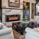 Rustic, modern great room features a stone fireplace and built-in cabinetry. Rustic wood beams balance modern custom drapes and furnishings.