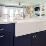 Kitchen remodel includes coastal, modern kitchen with fluted white porcelain sink in navy cabinets.