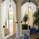 Dining room design includes custom arched window cornices with sheer curtains held by decorative wood hold backs.