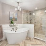 Coastal, shabby chic master bathroom features a free standing white bath tub set against tongue and groove, ship lap wall planks. The dramatic floor is porcelain tile adds rich tones of gray and beige and is set in a herringbone pattern.