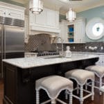 The island features an over sized stainless sink and industrial style faucet. along with coastal seeded glass pendants.