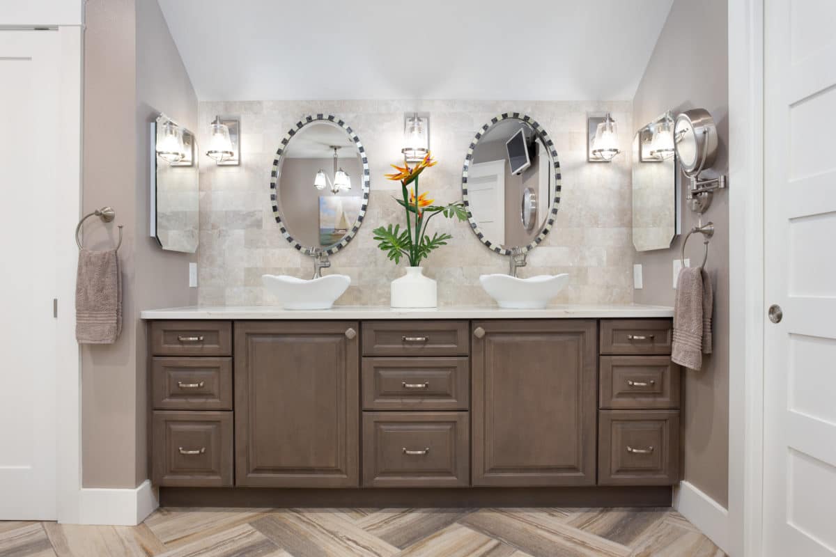 Bathroom decor includes coastal, shabby chic master bathroom has warm, weathered gray cabinets with tulip white vessel sinks all set against a backdrop of stone tile.