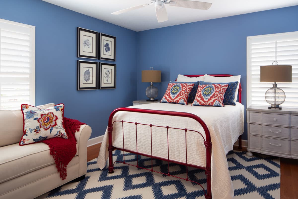 Bedroom decor includes custom pillows in shades of blue and red to compliment this vintage iron bed painted in a cherry red finish.
