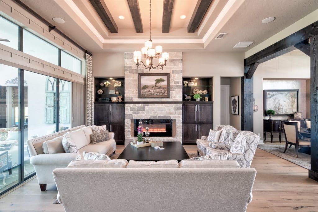 Interior design includes this rustic, modern great room featuring a stone fireplace and built-in cabinetry. Rustic wood beams balance modern custom drapes and furnishings.